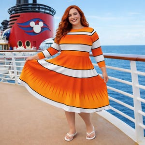 May include: A woman wearing a knee-length dress with orange and white horizontal stripes and a flared skirt. The dress has three-quarter sleeves and is paired with white sandals. The background shows a cruise ship deck and the ocean.