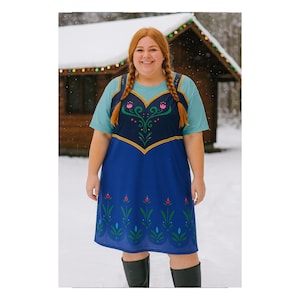 May include: A woman in a blue dress with a teal top. The dress features a dark blue bodice with gold trim and a floral design. The knee-length dress has a floral hem. She wears black boots and has red braids. The background is a snowy scene.