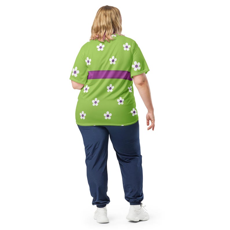 Puede incluir: Una camiseta verde lima con estampados de margaritas blancas y una franja horizontal morada. La camiseta se combina con pantalones de ch&aacute;ndal azul marino. El modelo lleva zapatillas blancas.