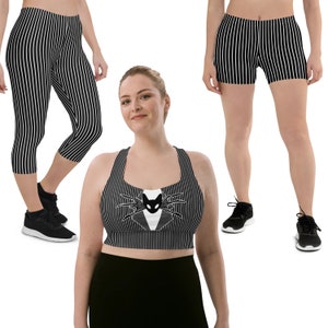 May include: A black and white striped sports bra with a black cat face graphic. The bra has a racerback style and is paired with black leggings and black shorts, also with a black and white striped pattern.
