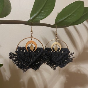 May include: A pair of black tassel earrings with gold crescent moon and leaf charms. The earrings are hanging from a branch.