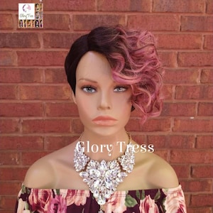 May include: A short, curly wig with black and pink hair. The wig is styled with a side part and the pink hair is curled and styled on one side. The wig is on a mannequin head wearing a floral print top and a large, sparkly necklace.