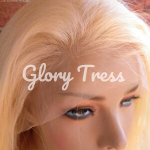 May include: A blonde human hair wig with a lace front. The wig is on a mannequin head and the lace front is visible. The wig is styled in a straight, long style.
