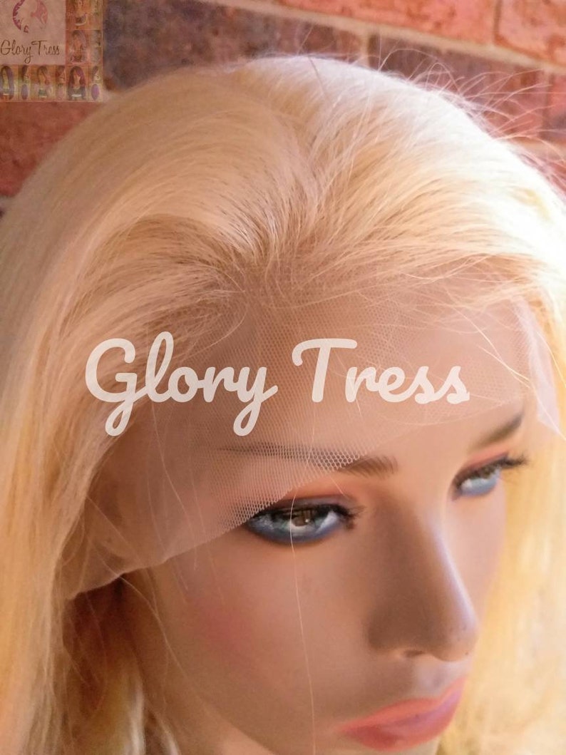 May include: A blonde human hair wig with a lace front. The wig is on a mannequin head and the lace front is visible. The wig is styled in a straight, long style.