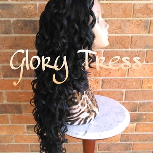 May include: A long, black, curly wig on a mannequin head. The wig is styled in loose curls and falls to the shoulders. The mannequin is wearing a leopard print scarf.
