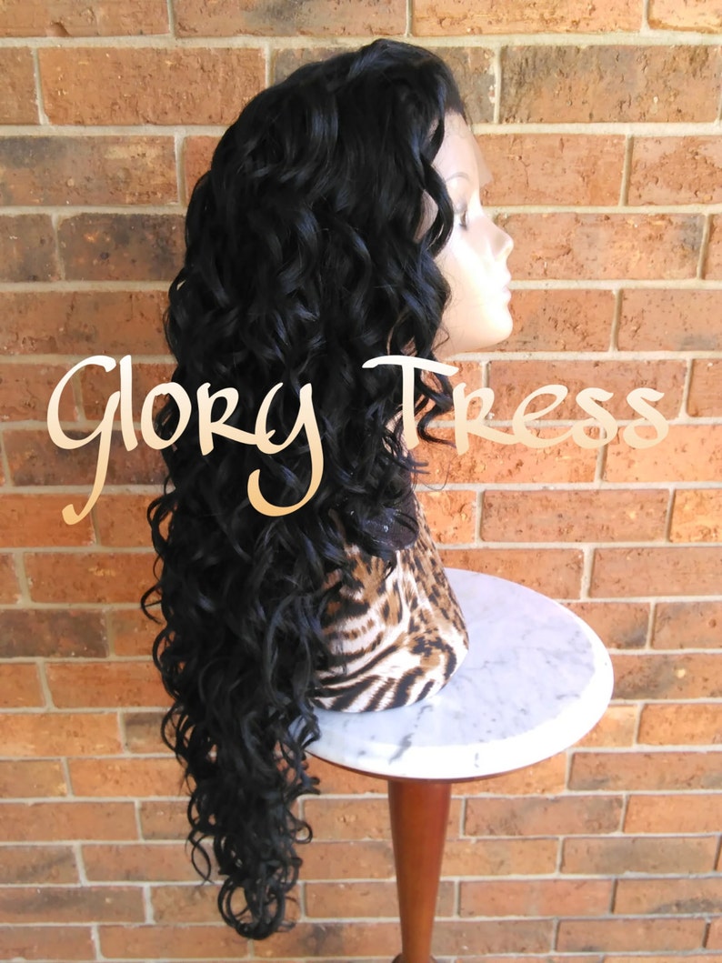 May include: A long, black, curly wig on a mannequin head. The wig is styled in loose curls and falls to the shoulders. The mannequin is wearing a leopard print scarf.