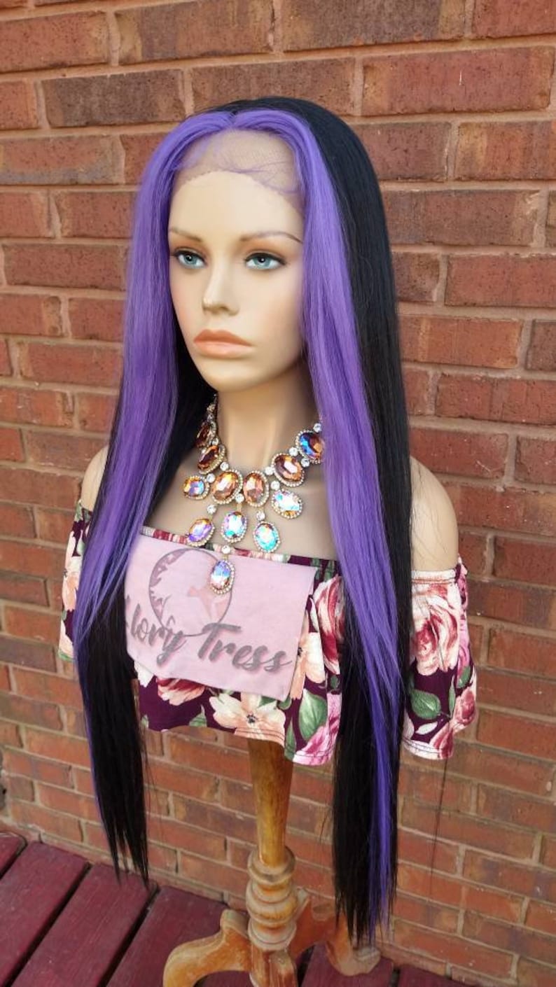 K&ouml;nnte beinhalten: Eine lange, glatte schwarze Per&uuml;cke mit violetten Str&auml;hnen. Die Per&uuml;cke ist mit einem Seitenscheitel gestylt und wird auf einem Mannequin-Kopf getragen. Das Mannequin tr&auml;gt ein Oberteil mit floralem Muster und einen gro&szlig;en, juwelenbesetzten Halsreif.