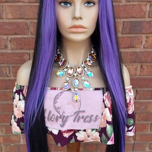 K&ouml;nnte beinhalten: Eine lange, gerade Per&uuml;cke mit schwarzen und violetten Haaren. Die Per&uuml;cke ist mit einem Mittelscheitel gestylt und die violetten Haare befinden sich an der Au&szlig;enseite der Per&uuml;cke. Die Per&uuml;cke sitzt auf einem Mannequin-Kopf und tr&auml;gt ein blumiges Hemd und eine gro&szlig;e, glitzernde Halskette.