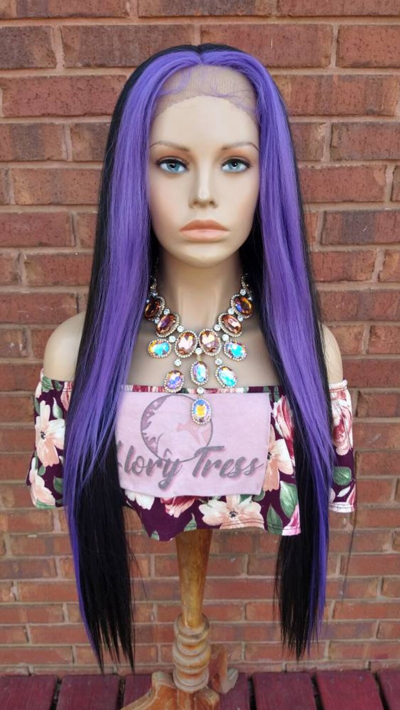 K&ouml;nnte beinhalten: Eine lange, gerade Per&uuml;cke mit schwarzen und violetten Haaren. Die Per&uuml;cke ist mit einem Mittelscheitel gestylt und die violetten Haare befinden sich an der Au&szlig;enseite der Per&uuml;cke. Die Per&uuml;cke sitzt auf einem Mannequin-Kopf und tr&auml;gt ein blumiges Hemd und eine gro&szlig;e, glitzernde Halskette.