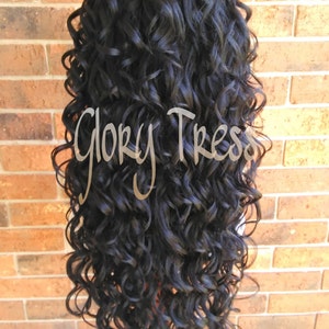 May include: A long, black curly wig on a wig stand. The wig is styled in loose, bouncy curls.