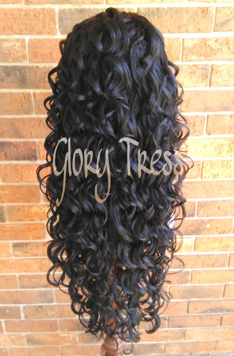 May include: A long, black curly wig on a wig stand. The wig is styled in loose, bouncy curls.