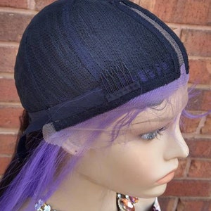 K&ouml;nnte beinhalten: Eine lila und schwarze Per&uuml;cke mit einem Spitzenfront und verstellbaren Tr&auml;gern. Die Per&uuml;cke ist in einem langen, geraden Stil gestylt. Die Per&uuml;cke befindet sich auf einem Mannequin-Kopf mit einer Juwelenkette.