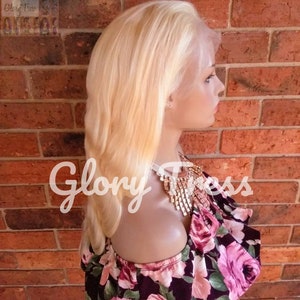 May include: A platinum blonde human hair wig with a lace front. The wig is styled in a straight, shoulder-length cut. The wig is on a mannequin head and is displayed against a brick wall.