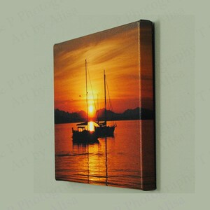 May include: A canvas print of a sunset over the ocean with two sailboats silhouetted against the orange and red sky.
