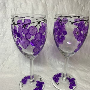 Puede incluir: Dos copas de vino de vidrio transparente con uvas moradas pintadas sobre ellas. Las uvas están pintadas en racimo con vides negras.