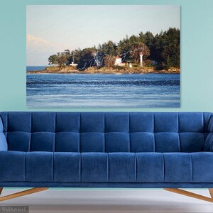 May include: A white lighthouse on a small island with trees and a blue sky. The water is calm and blue.