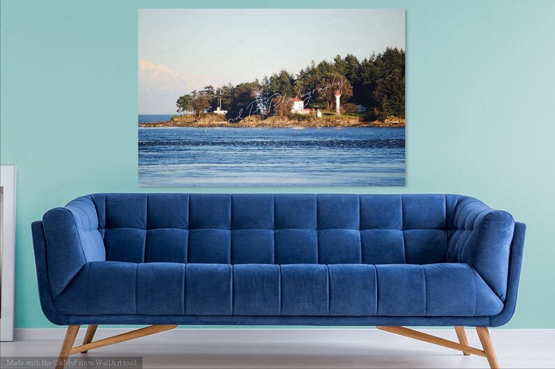 May include: A white lighthouse on a small island with trees and a blue sky. The water is calm and blue.