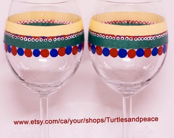 Puede incluir: Dos copas de vino de vidrio transparente con diseños pintados a mano. Las copas tienen un patrón amarillo, verde, rojo y azul con puntos blancos.