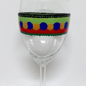 Puede incluir: Una copa de vino de vidrio transparente con un dise&ntilde;o pintado a mano. El dise&ntilde;o presenta una banda negra con c&iacute;rculos verdes, rojos, amarillos y azules.