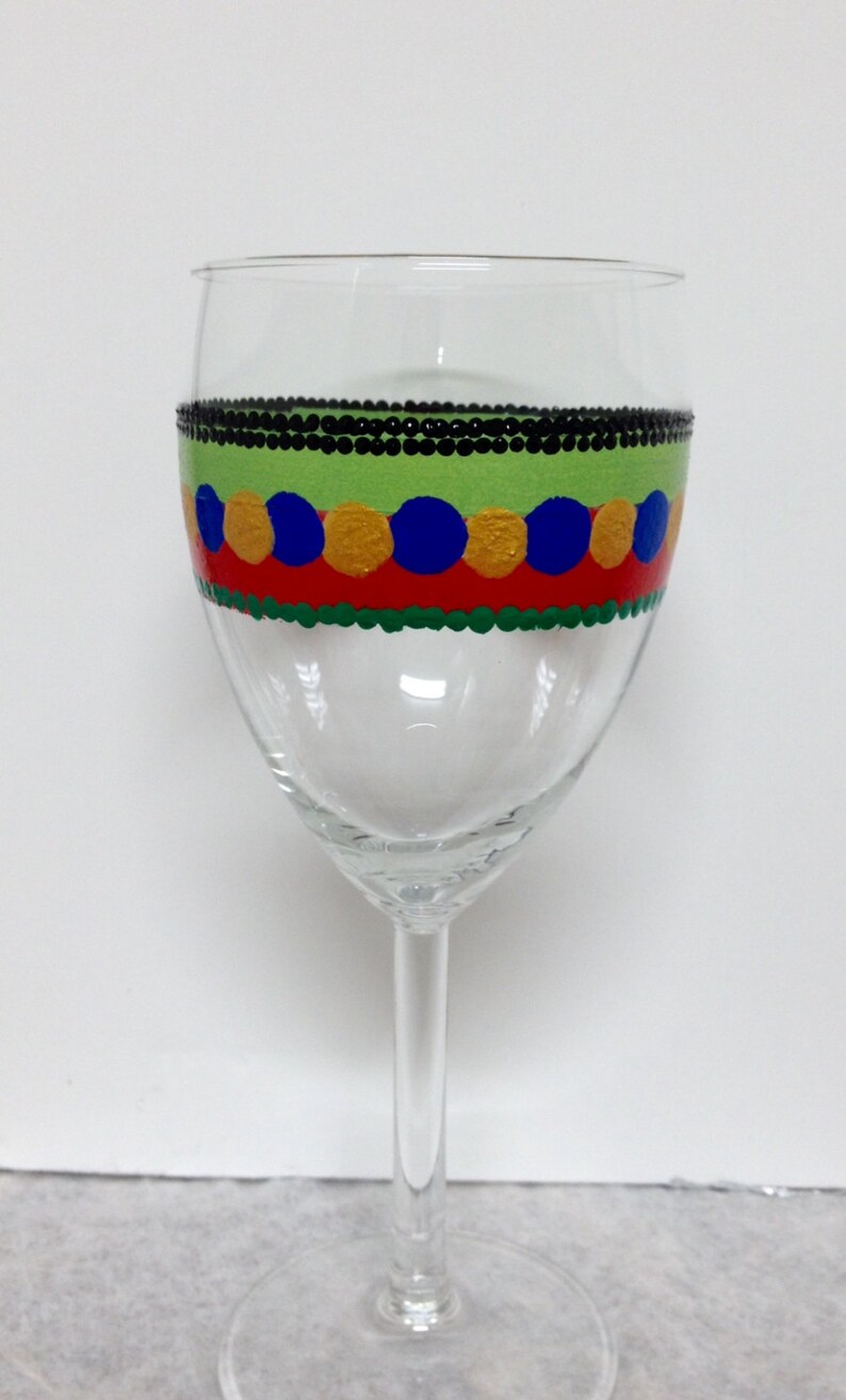 Puede incluir: Una copa de vino de vidrio transparente con un dise&ntilde;o pintado a mano. El dise&ntilde;o presenta una banda negra con c&iacute;rculos verdes, rojos, amarillos y azules.