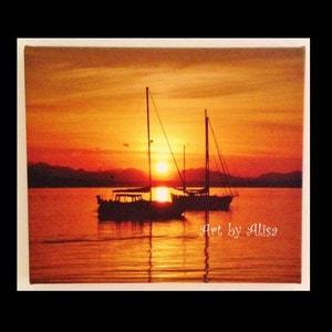 May include: Two sailboats silhouetted against a vibrant orange sunset over a calm body of water. The sky is a mix of orange, yellow, and red hues, creating a dramatic backdrop for the scene. The text "Art by Alisa" is visible in the lower right corner of the image.