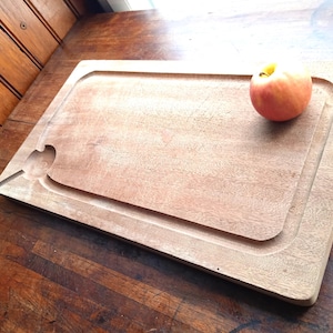 Può includere: Un tagliere rettangolare in legno con una scanalatura per il succo e un ritaglio a forma di uccello. Una mela rossa e gialla è sul tagliere. Il tagliere è in legno marrone chiaro e su una superficie di legno marrone scuro.