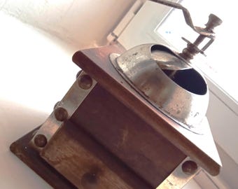 Puede incluir: Un molinillo de café vintage de madera con una manivela de metal y un mecanismo de molienda de metal. El molinillo tiene un cajón para recoger el café molido.