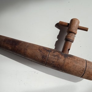 Op de afbeelding: Een houten vatenkraan met een lange, cilindrische tuit en een handvat met een kruisvormige bovenkant.