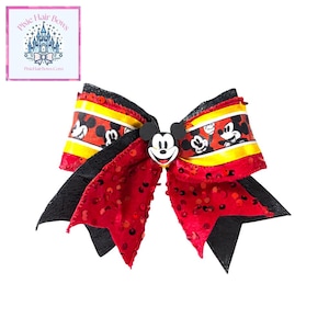 May include: A large, decorative hair bow featuring a Mickey Mouse design. The bow has red, black, yellow, and white accents, with a Mickey Mouse character embellishment. The bow has a sequined red center and black tails. The text "Pixie Hair Bows" is in the upper left corner.