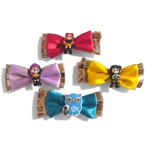 May include: Five colorful hair bows with character figures. Each bow features a satin bow in pink, purple, yellow, and teal, with a gold glitter accent. The bows are adorned with small figurines of cartoon characters.
