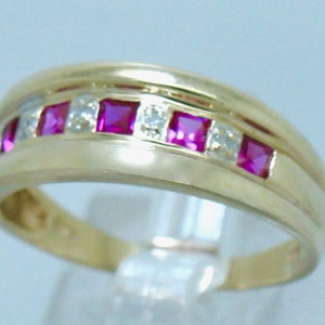 May include: A gold band ring with a row of alternating red rubies and clear diamonds.