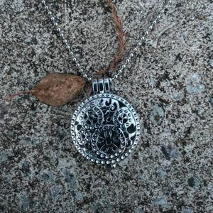 May include: A silver chain necklace with a round pendant featuring a detailed floral design. The pendant is attached to the chain with a silver loop.