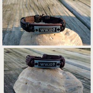 May include: A brown leather bracelet with black braided cord and a silver metal tag that reads "WWJD?" The bracelet is on a rock.
