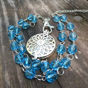 May include: A silver locket with a delicate floral design hangs from a chain with light blue glass beads.