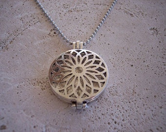 May include: Silver necklace with a round pendant featuring a detailed, intricate floral design. The pendant is open and has a hinged closure.