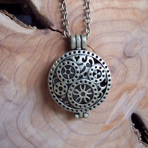 May include: A bronze pendant necklace with a round, openwork charm featuring a floral design. The charm has a filigree pattern with multiple circles and a central flower.