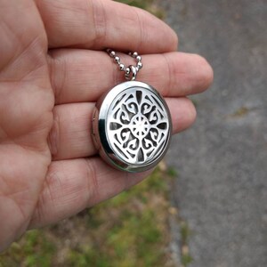 May include: A silver pendant necklace with a round, openwork design. The pendant has a filigree pattern and is attached to a silver chain.