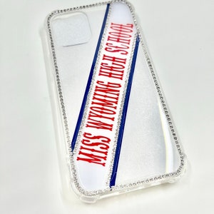 May include: A clear phone case with a white and blue sash that says "Miss Wyoming High School" in red letters. The case is decorated with a border of rhinestones.