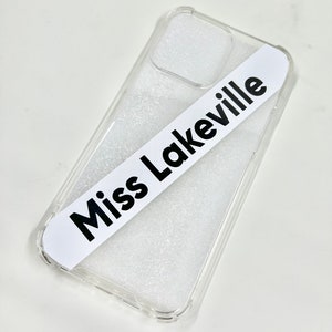 May include: Clear phone case with a white sticker that says "Miss Lakeville" on it.