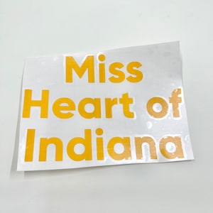 May include: A white sticker with the text "Miss Heart of Indiana" in yellow letters.