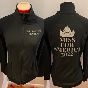 May include: Black zippered jacket with the text "DR. RACHEL FENTERS" on the left side and "MISS FOR AMERICA 2022" with a crown graphic on the right side.
