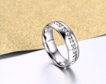 May include: A silver band ring with a row of clear cubic zirconia stones around the centre.
