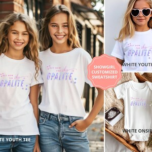May include: White youth tees and a white onesie with the text "But now the sky is Opalite" in a gradient of pink and blue. The image also shows a customized sweatshirt.
