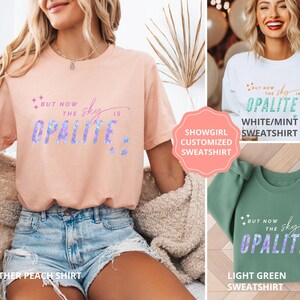 May include: A heather peach t-shirt with the text "But now the sky is Opalite" in a gradient font. The image also shows a white and mint sweatshirt and a light green sweatshirt with the same text.