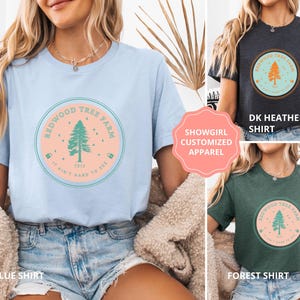 Pode incluir: Camisetas azul claro, cinza escuro e verde floresta. Cada uma apresenta um gr&aacute;fico circular com o texto "Redwood Tree Farm" e uma ilustra&ccedil;&atilde;o de &aacute;rvore. O texto "It ain't hard to see" tamb&eacute;m est&aacute; inclu&iacute;do.