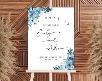 May include: A white wedding welcome sign with blue watercolor flowers and greenery. The text reads "Welcome to the wedding of Emily and Asher, Saturday June 10, 20XX, Hudson, NY".