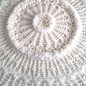 May include: White crocheted doily with a circular design and a fluffy white border.