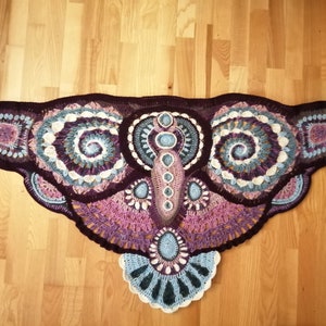 Peut inclure: Un châle en crochet aux nuances de violet, rose, bleu et blanc, en forme de papillon avec des détails complexes.
