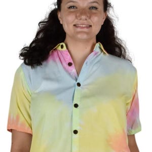 May include: A short-sleeved shirt with a tie-dye design in pastel shades. The shirt displays a gradient of yellow, pink, and blue. It has a traditional collar and dark brown buttons.