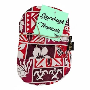 May include: A red, white, and burgundy patterned bread bag with the text "Sourdough Tropicale" on a light green tag. The bag is tied with twine and has a small black "ALOHA" tag.